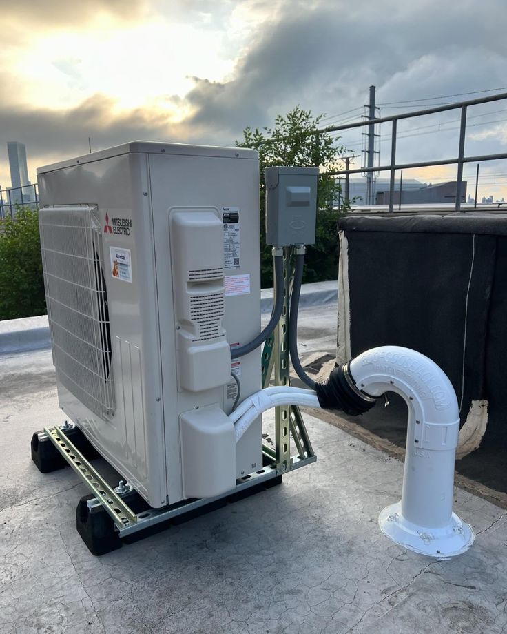 An dreamvil air source heat pump outdoor unit covered in snow with snow on the ground. It is placed against a wall, between some potted plants